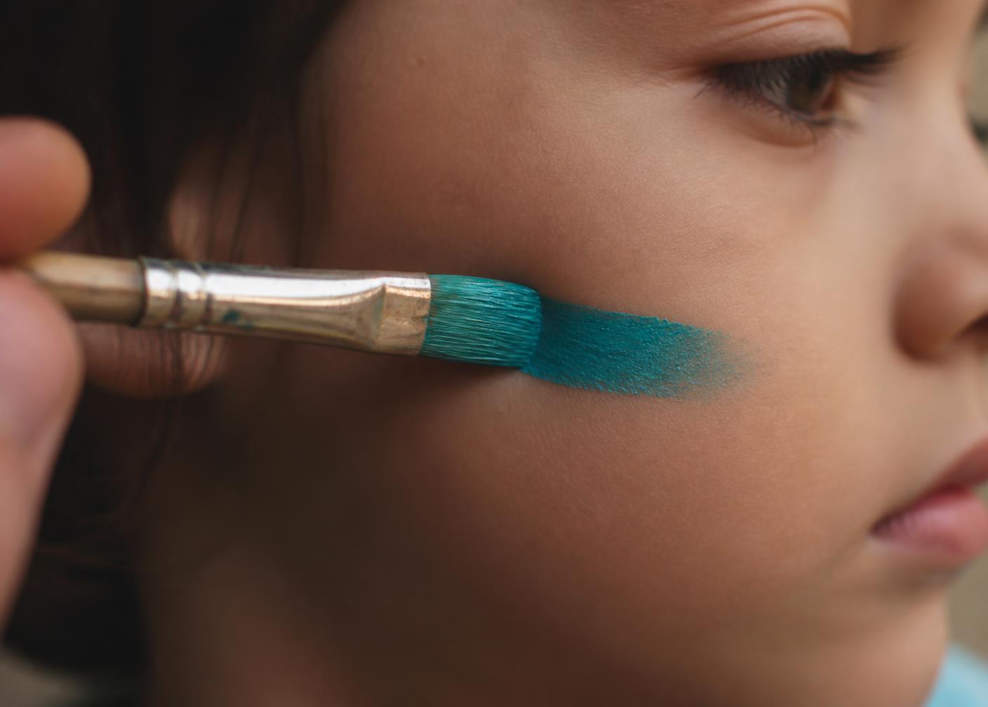 Close detail of a brush laying turquoise paint on skin at a corporate family day